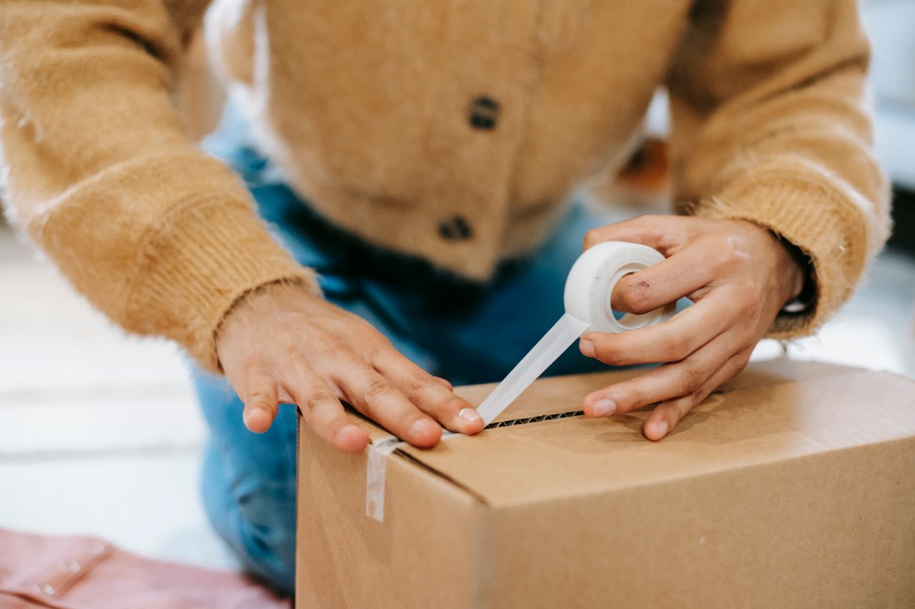 Hands sealing a cardboard parcel with tape.